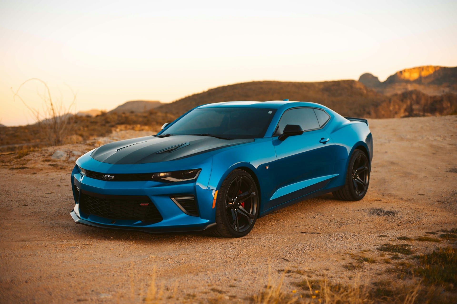 Blue coupe with a contrasting black bonnet and roof, parked at sunset